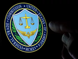 FTC Federal Trade Commission logo seen on the display in a dark room and blurred finger pointing at it