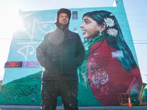 Artist Victor MARKA27 Quinonez poses before his mural on Bangladeshi life on the side of Bridge Academy West in Detroit Michigan. (Image via Imagn / USA Today images)