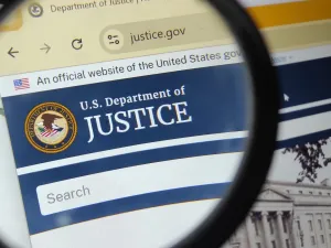 Department of Justice website under a magnifying glass (Image via Shutterstock.com)