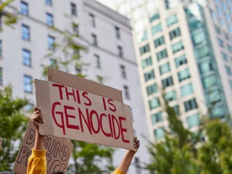 Women holding sign "this is genocide" written in red marker