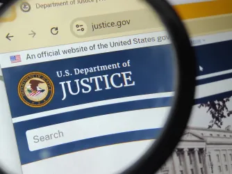 Department of Justice website under a magnifying glass (Image via Shutterstock.com)