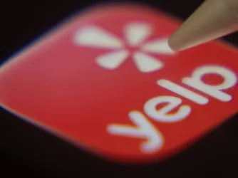 Close-up of the Yelp app on a screen with a stylus pointing at it. (Image via Shutterstock.com)