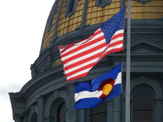Colorado state capitol with US and Colorado flags in foreground (Image via Shutterstock.com)
