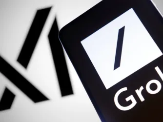 xAI logo in the background with a smartphone in the phone ground with the Grok logo.