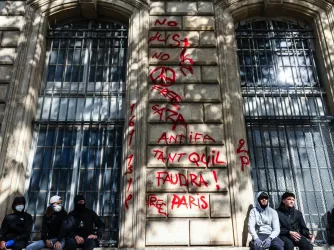 French youth sit on the side of the street against a wall covered in graffiti during the France riots in Paris