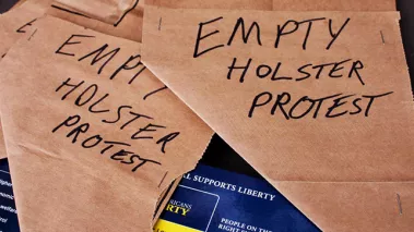 Folded brown paper bags with the words "Empty holster protest" written in black marker on the side