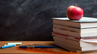 An apple atop a stack of school books on a desk