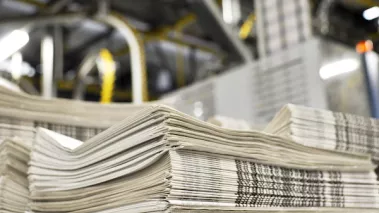 stack of freshly printed daily newspapers transported to a printing plant, in the background machines and technical equipment of a large printing plant