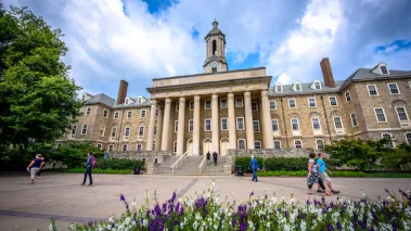 Students and adults walk in front of the Old Main building, on the campus of Penn State University, in State College, Pennsylvania.
