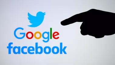 Silhouette of hand pointing Twitter Google Facebook logos on the blurred screen 