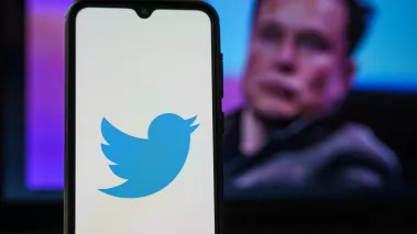 Phone with Twitter icon and Elon Musk in background