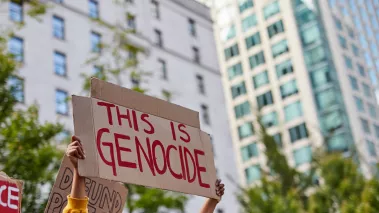 Women holding sign "this is genocide" written in red marker