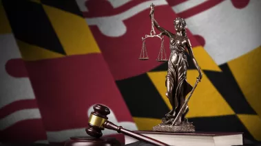 Maryland state flag with statue of lady justice and judge gavel on black drapery