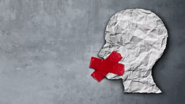 wrinkled piece of paper cut out to look like a human head with red tape over the mouth
