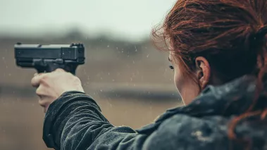Woman with hair pulled back aiming a gun down range