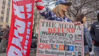 Pro-Trump protester in New York holding sign that reads: "Defund the Media" and has logos of ABC, NPR, and other news outlets.
