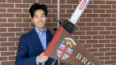 Alex Shieh holding a chainsaw and a Brown University pennant