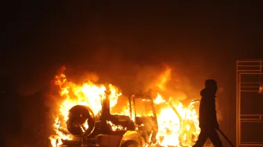 Protester walks past a burning car