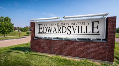 Brick sign alongside road with campus buildings in background at Southern Illinois University Edwardsville