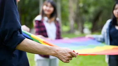 College students holding a rainbow pride flag together on a college campus