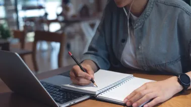Student seated at laptop taking notes.