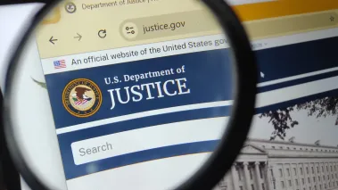 Department of Justice website under a magnifying glass (Image via Shutterstock.com)