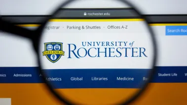 University of Rochester website homepage visible on display screen under magnifying glass (Image via Shutterstock.com)