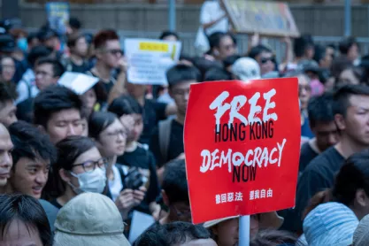 Photo of a pro-democracy protest in Hong Kong with a red sign reading: "Free Hong Kong Democracy Now"