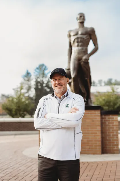 FIRE plaintiff Michael Balow standing outside in front of a sculpture with his arms crossed.