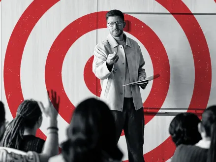 Graphic showing a black and white photo of a teacher at the front of a classroom filled with students with a red bullseye target over the teacher