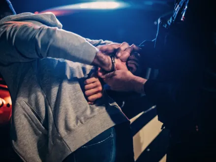 Police officer handcuffing man on hood of police car (Image via Shutterstock.com)