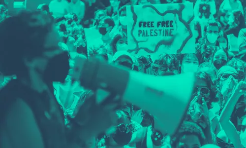 Person speaking into a megaphone in the foreground and a crowd of people in the background.