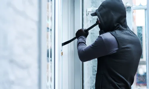Criminal wearing black hoodie with crowbar breaking into house (Image via Shutterstock.com)