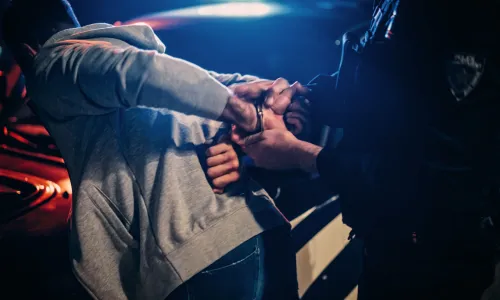 Police officer handcuffing man on hood of police car (Image via Shutterstock.com)