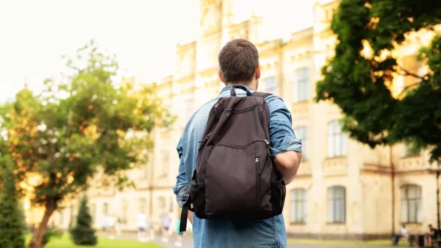 Student university standing with his back to the camera and his backpack on one shoulder and walking in university campus