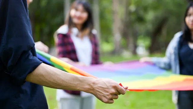 College students holding a rainbow pride flag together on a college campus