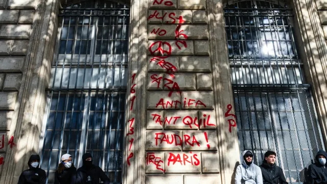 French youth sit on the side of the street against a wall covered in graffiti during the France riots in Paris
